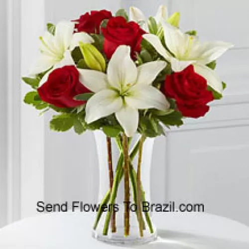Rosas vermelhas e lírios brancos com alguns complementos sazonais em um vaso de vidro
